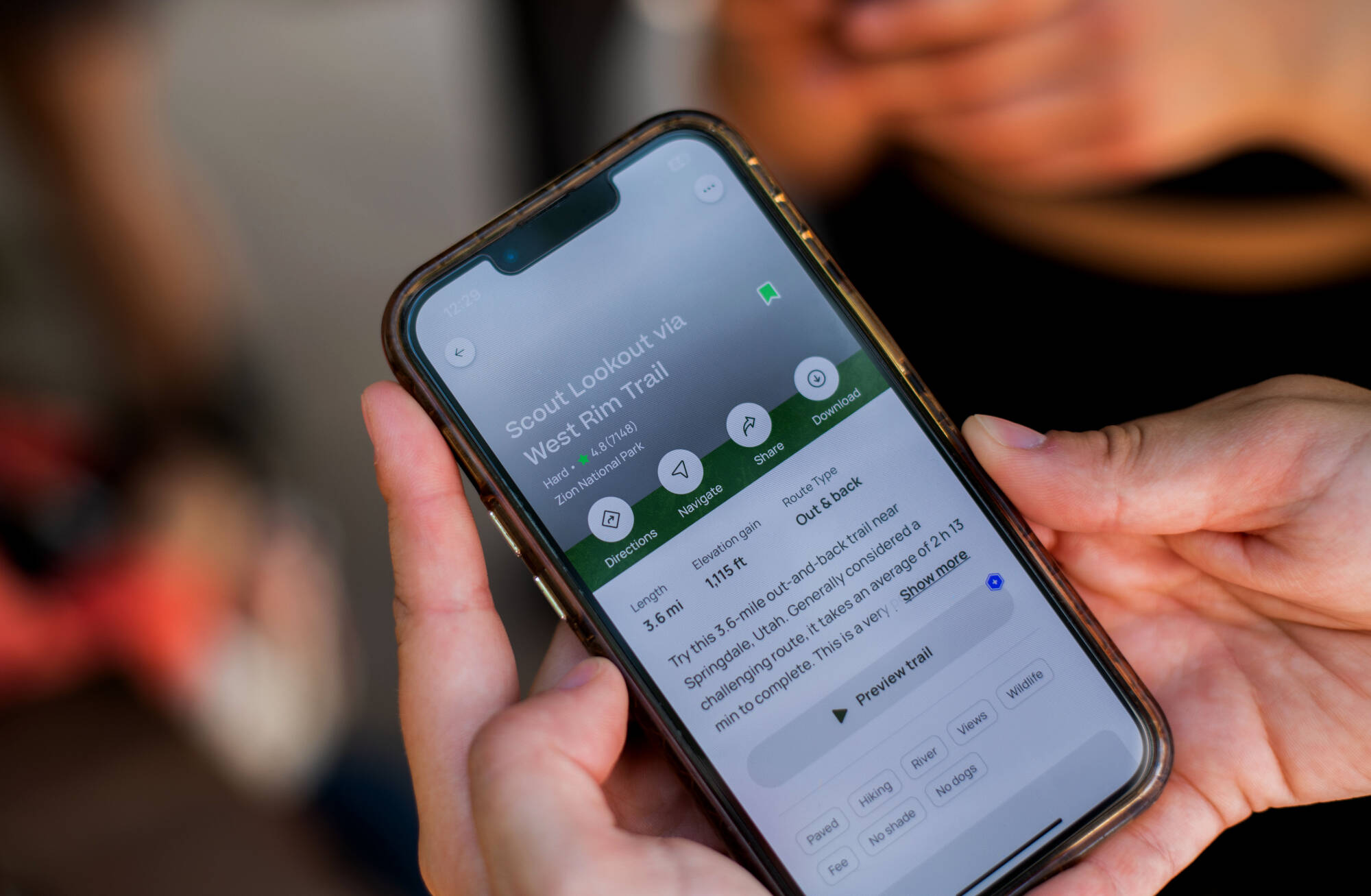 A student holds their cell phone showing the details about the trail they are about to hike at Zion National Park.